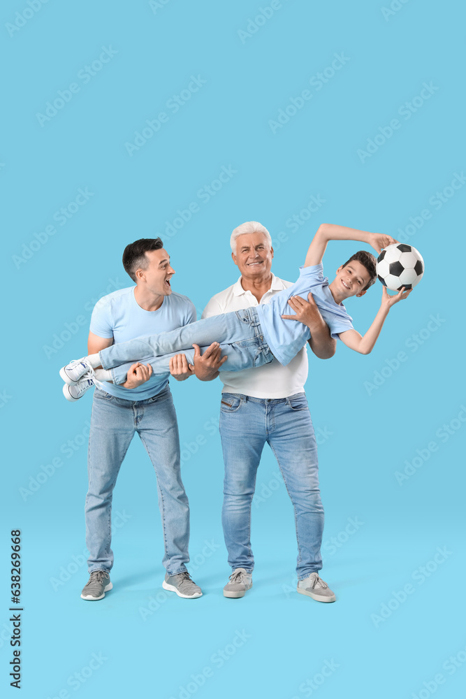 Fototapeta premium Little boy with his dad and grandfather holding soccer ball on blue background