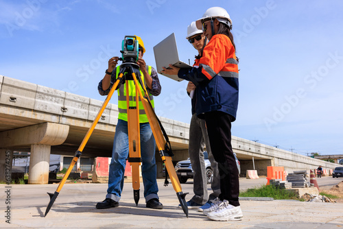 Engineer use theodolite equipment and looking blueprints project on laptop for route surveying to build a bridge across the intersection to reduce traffic congestion during rush hours