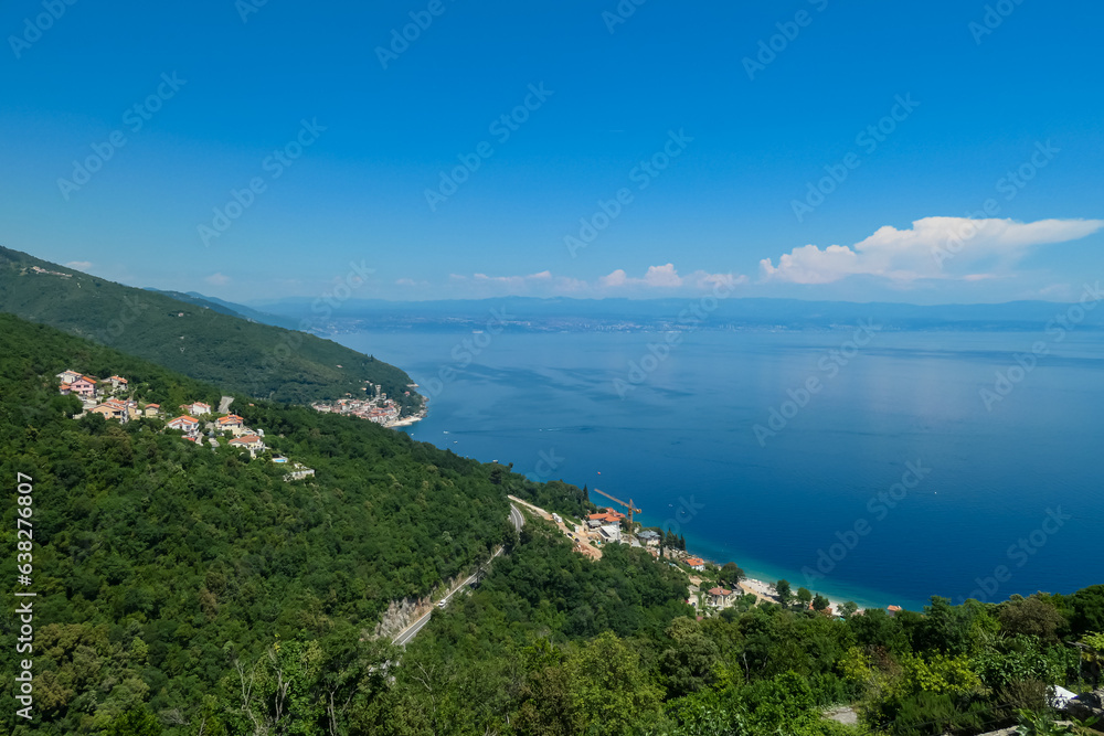 A panoramic view from above of the shore along Moscenicka Draga, Croatia. A few small towns located on the shore of the Mediterranean Sea. Lush green hills along the hills. Sunny day.