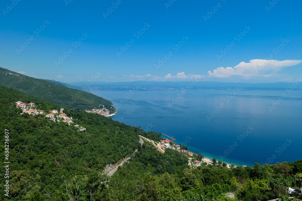 A panoramic view from above of the shore along Moscenicka Draga, Croatia. A few small towns located on the shore of the Mediterranean Sea. Lush green hills along the hills. Sunny day. A panoramic view from above of the shore along Moscenicka Draga, Croatia. A few small towns located on the shore of the Mediterranean Sea. Lush green hills along the hills. Sunny day.