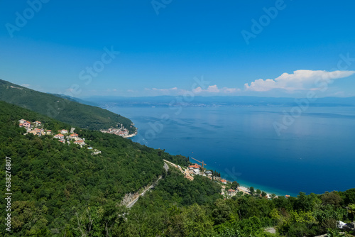 A panoramic view from above of the shore along Moscenicka Draga, Croatia. A few small towns located on the shore of the Mediterranean Sea. Lush green hills along the hills. Sunny day.