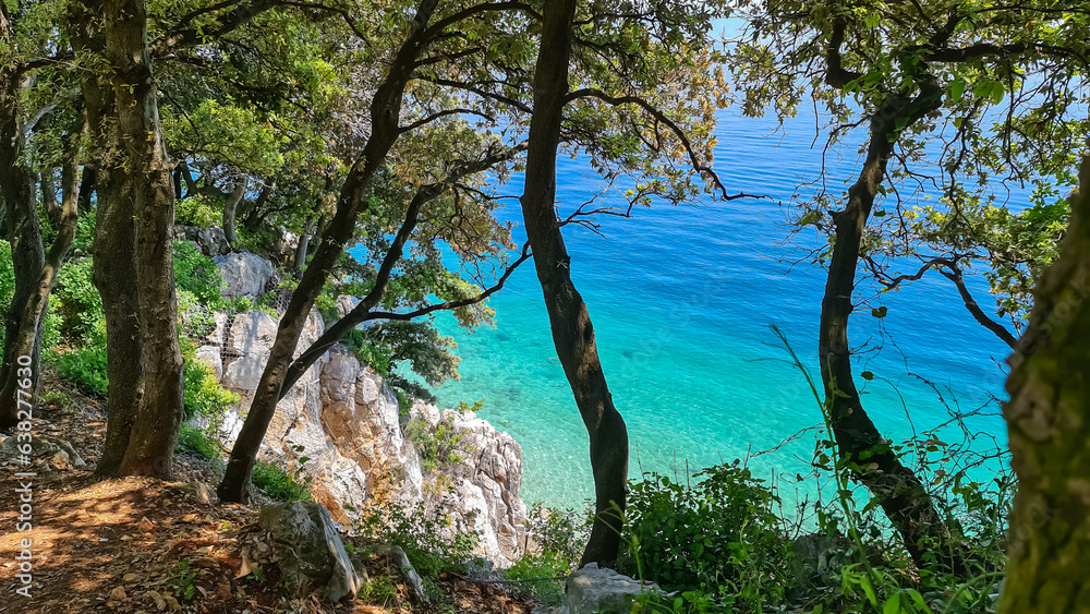 A view on the seashore from a cliff above the beach in Croatia. The sea has turquoise color and is very clean. There are a few trees growing on the steep cliffs. Stony beach. Sunny and warm day.
