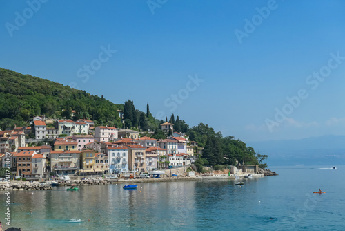 A close up on the shore along Moscenicka Draga, Croatia. There is a small town located on the shore of the Mediterranean Sea. Few boats crossing the calm sea. Green hills in the back. Summer vibes.