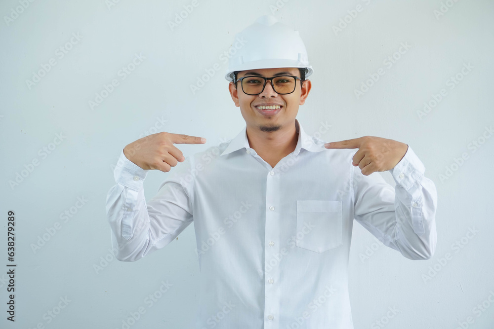 Young asian architect man wearing builder safety helmet smiling with happy face looking and pointing him self isolated on white background Young asian architect man wearing builder safety helmet smiling with happy face looking and pointing him self isolated on white background