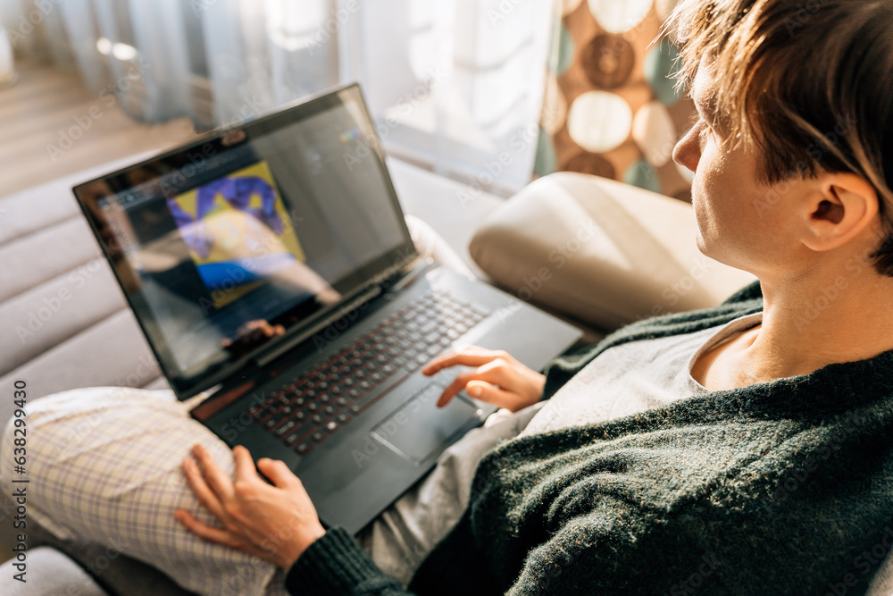 Fototapeta premium A woman uses a laptop at home sitting on the couch