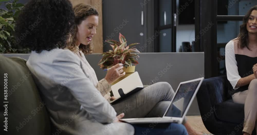 Diverse female colleagues in discussion using laptop and tablet in office lounge, slow motion Diverse female colleagues in discussion using laptop and tablet in office lounge, slow motion