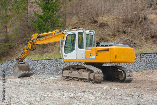 A crawler excavator with a rotating house platform and continuous caterpillar track, and a scoop bucket. On a site near Forni Avoltri in Carnia, Udine, Friuli-Venezia Giulia, N.E. Italy