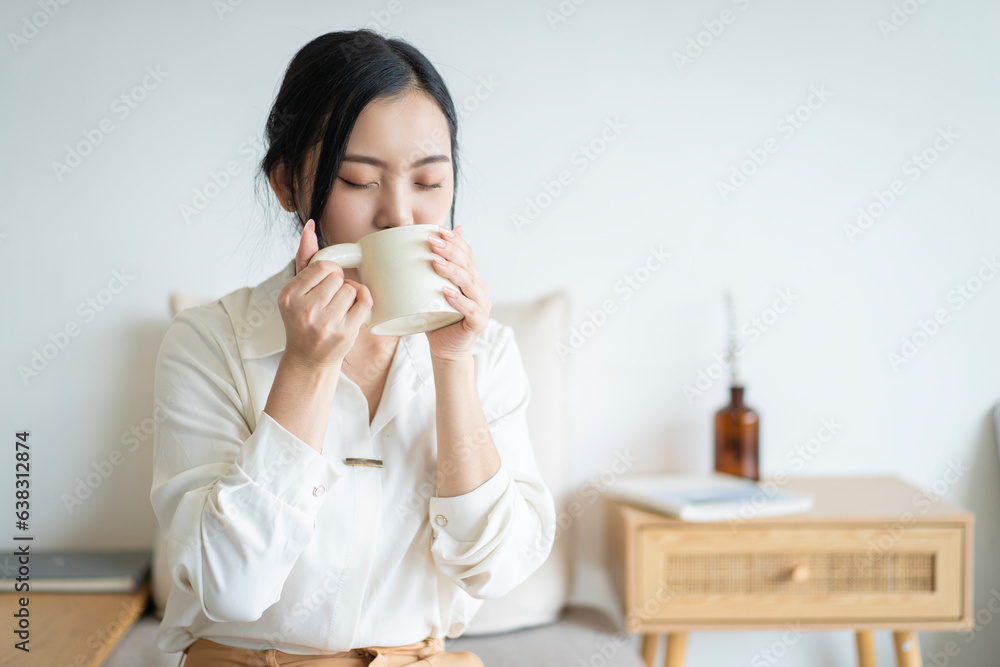 Young woman at home sitting on modern chair relaxing with hot water Young woman at home sitting on modern chair relaxing with hot water