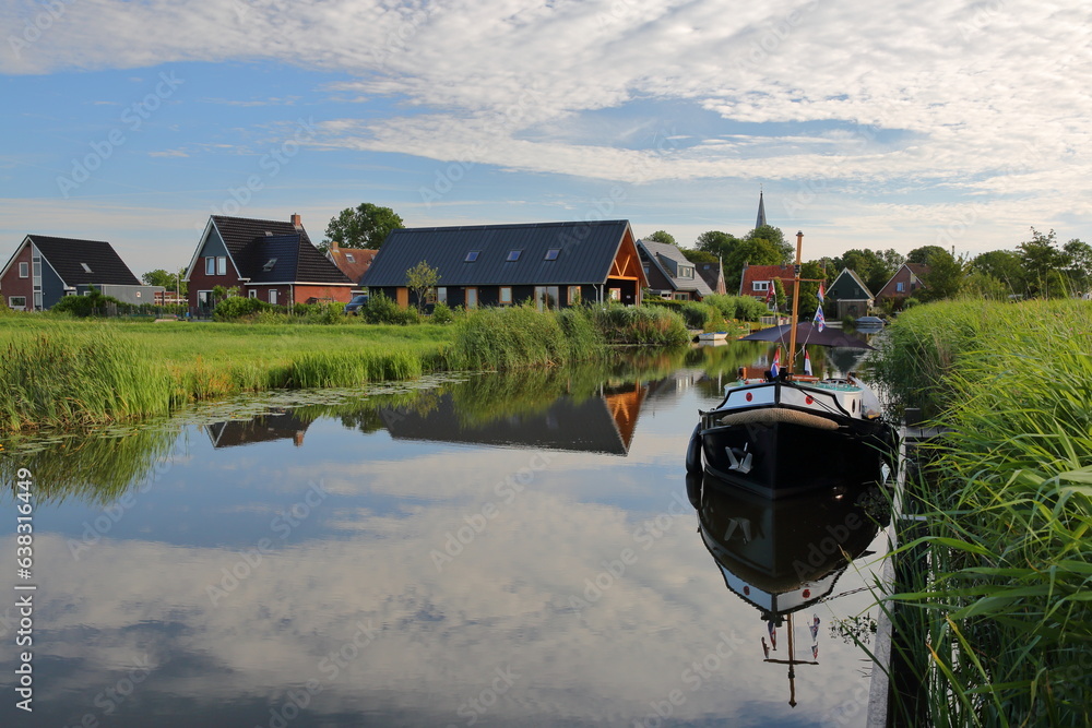 Reflection of houses and a mooring boat along a canal in Baard, Friesland, Netherlands, a small village located 13km West from Leeuwarden
