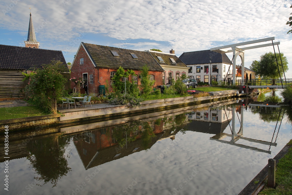 Reflection of houses and a drawbridge along a canal in Baard, Friesland, Netherlands, a small village located 13km West from Leeuwarden, with the bell tower of the church on the left