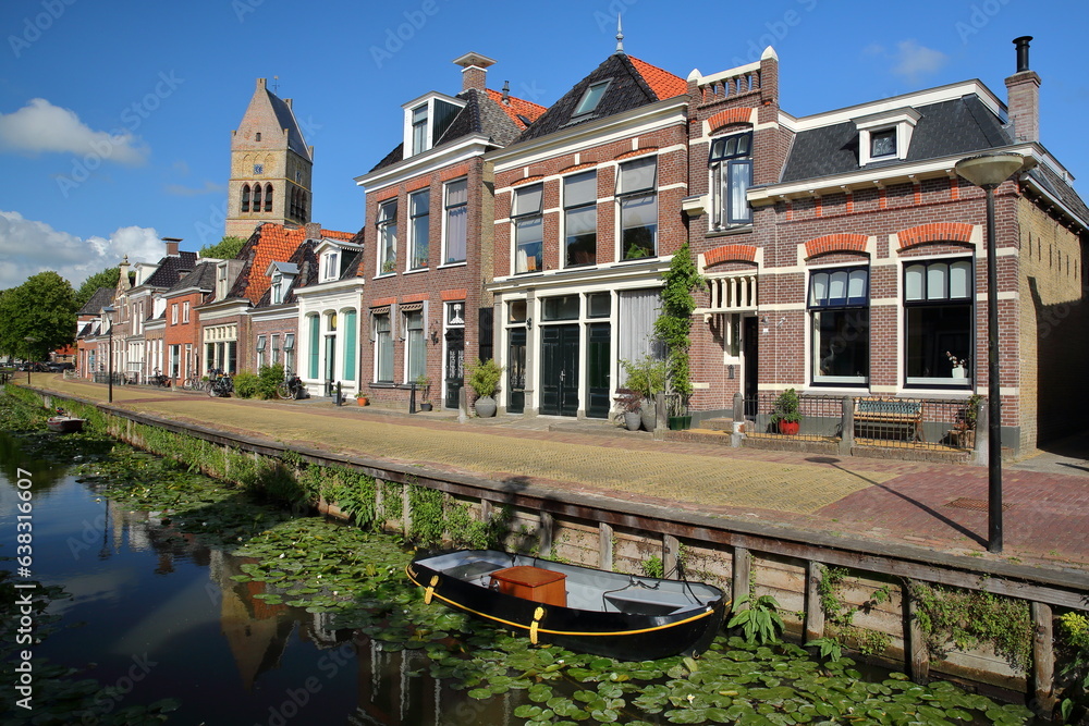 Reflections of colorful house facades along Kleine Dijlakker street in Bolsward, Friesland, Netherlands, with the bell tower of Martinikerk (St Martin church) in the background