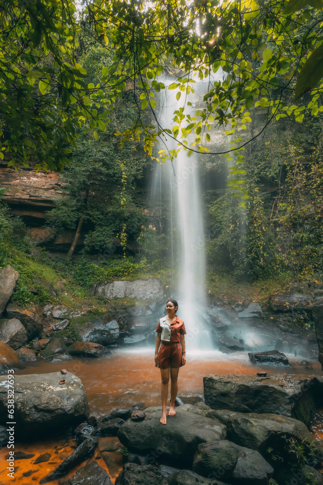 A young beautiful Asian girl explores a waterfall during her summer vacation in Laos, Asia