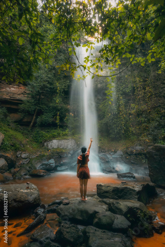 A young beautiful Asian girl explores a waterfall during her summer vacation in Laos, Asia