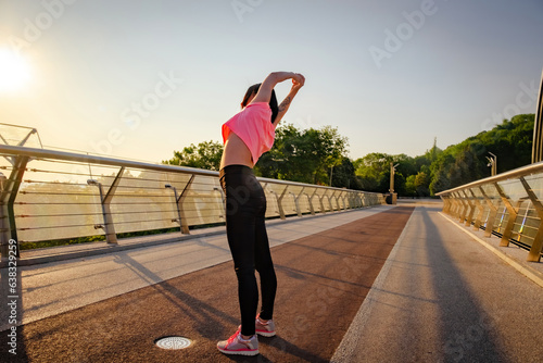 Young lady in tracksuit leans torso to side on glass bridge. Sunny day gives energy and strength to carry out successful workout © SlavaStock