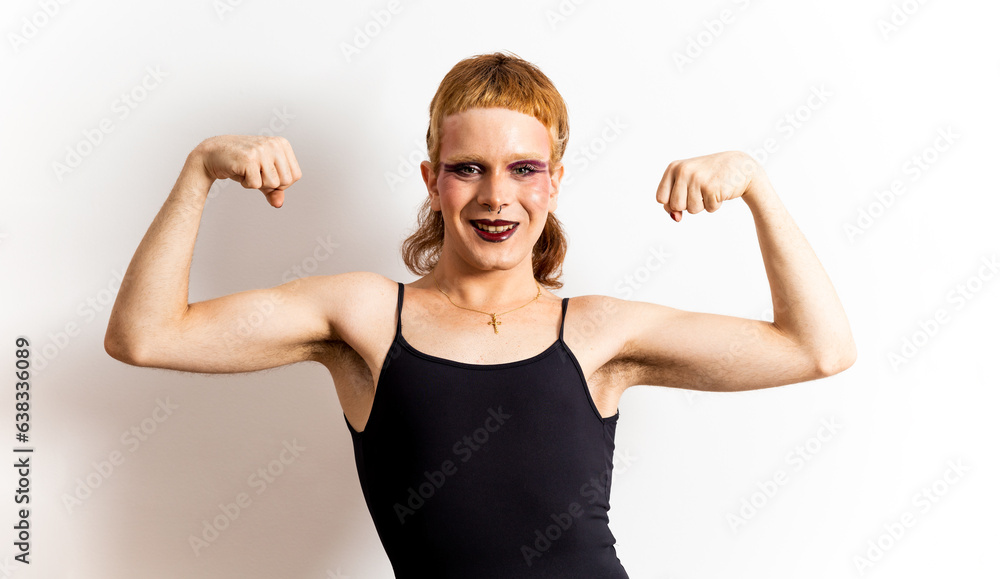 A red-haired non-binary person wearing makeup in a black T-shirt poses on a white background while showing off both biceps. Concept of support for the LGBTI collective, strength for LGBT people. A red-haired non-binary person wearing makeup in a black T-shirt poses on a white background while showing off both biceps. Concept of support for the LGBTI collective, strength for LGBT people.