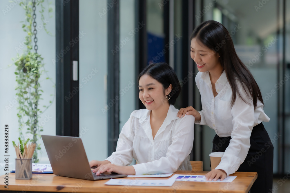 Two cheerful Asian office workers women collaborating on a project sitting at desk with laptop computer. Two cheerful Asian office workers women collaborating on a project sitting at desk with laptop computer.