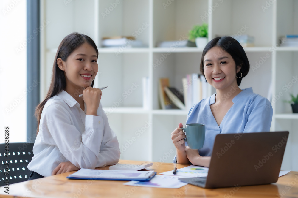 Two cheerful Asian office workers women collaborating on a project sitting at desk with laptop computer. Two cheerful Asian office workers women collaborating on a project sitting at desk with laptop computer.
