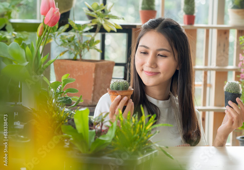 Portrait garden beautiful pretty young Asian girl woman wearing white blouse with long black hair and smile fresh with bright smile  look pot small tree leaf green plant in room shop Happy and relax