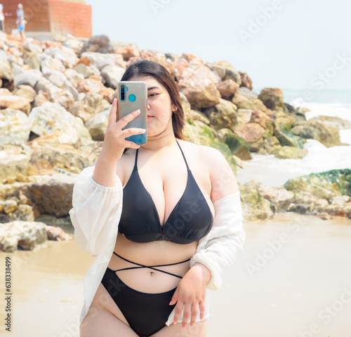 Portrait young woman asian chubby cute beautiful taking pictures with smartphone in bikini black sexy front viewpoint tropical sea beach white sand clean and bluesky calm Nature ocean Beautiful wave
