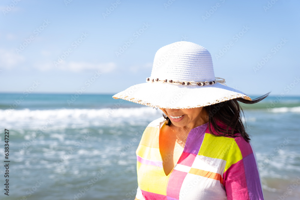 Smiling unrecognizable woman in hat and colorful flashy dress enjoying a lovely walk along the seashore on a bright spring morning.