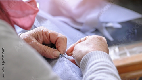 Close-up of a elderly woman sews by hand with a needle and thread. Selective focus.