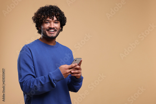 Handsome smiling man using smartphone on beige background, space for text