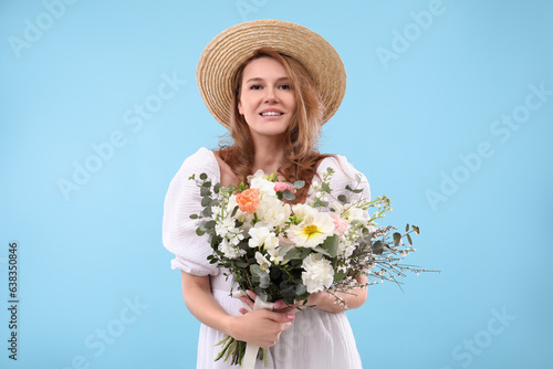Beautiful woman in straw hat with bouquet of flowers on light blue background
