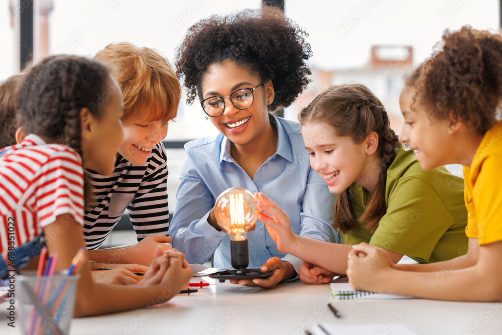 Multiethnic teacher and kids studying electricity and incandescent light bulb at physics lesson. - obrazy, fototapety, plakaty 