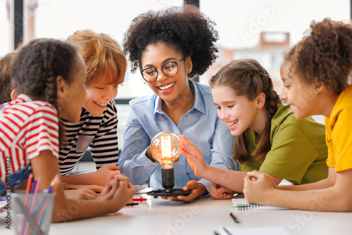 Multiethnic teacher and kids studying electricity and incandescent light bulb at physics lesson. © JenkoAtaman