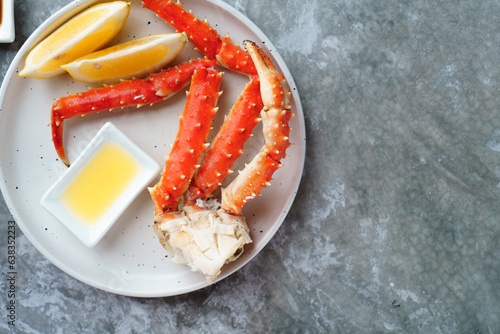 Red king crab legs with butter sauce and lemon wedges on a white plate, selective focus.