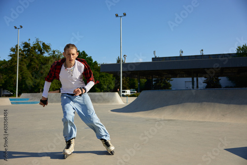 Trendy fashioned teenage guy rollerblading at urban skating park photo