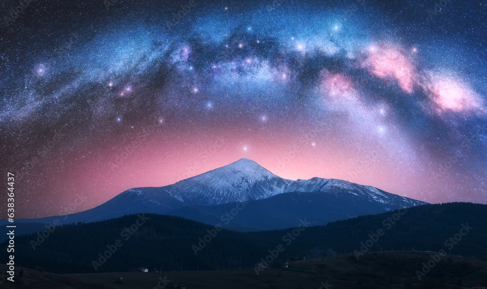Arched Milky Way over the beautiful mountains with snow covered peak at night in summer. Colorful landscape with bright starry sky with Milky Way arch, snowy rocks, hills, pink light. Space. Nature