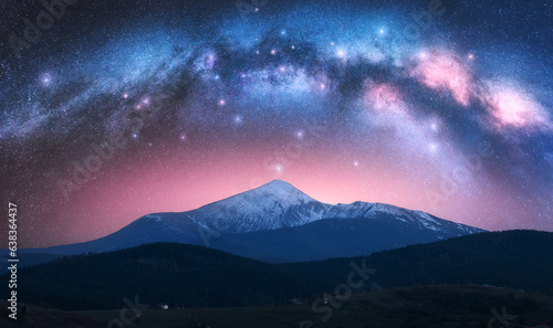 Arched Milky Way over the beautiful mountains with snow covered peak at night in summer. Colorful landscape with bright starry sky with Milky Way arch  snowy rocks  hills  pink light. Space. Nature