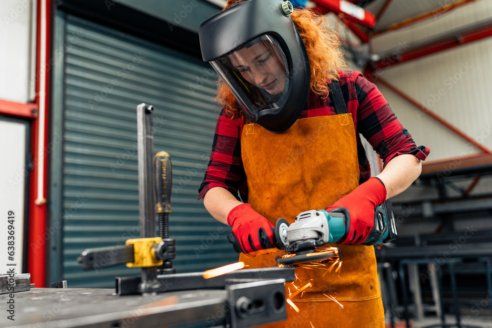 Fototapeta premium A self-taught girl grinds in the workshop, uses a visor and gloves for protection