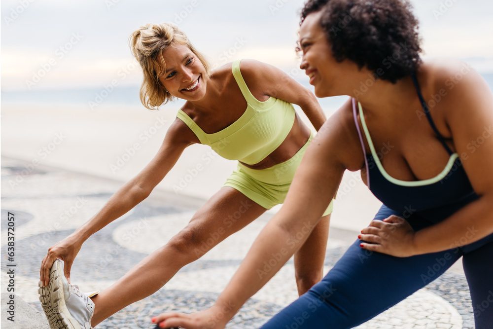 Happy women doing stretch exercises during a beach workout session Happy women doing stretch exercises during a beach workout session