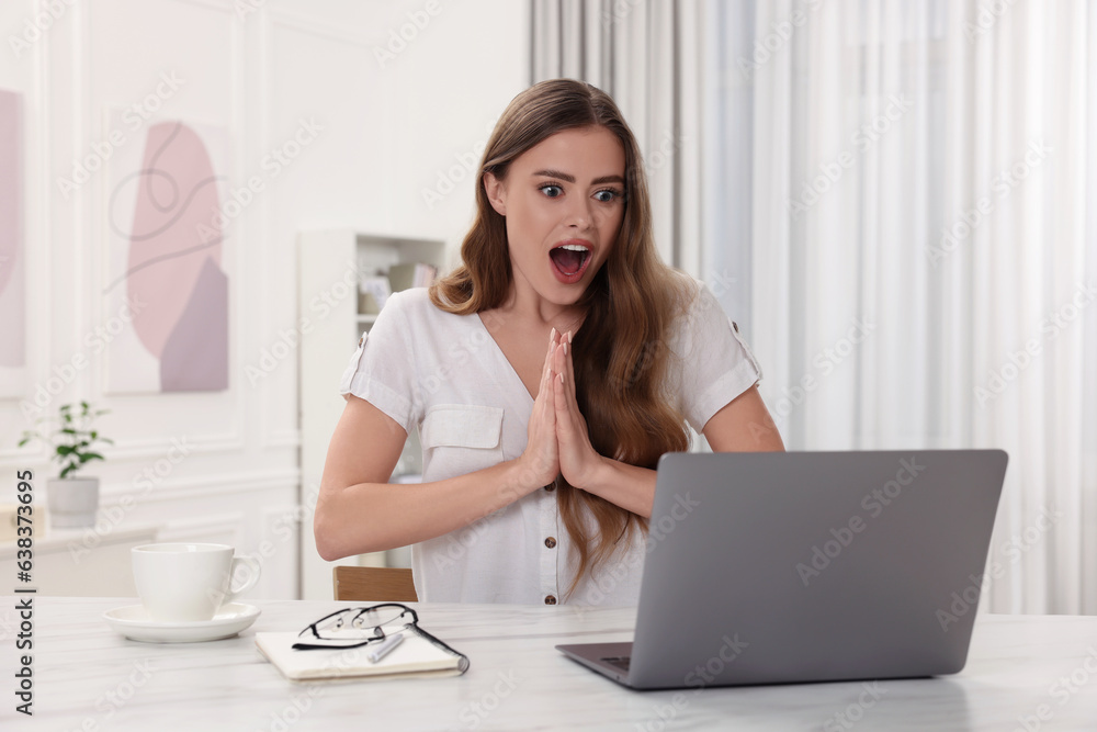 Surprised woman using laptop at white table in room Surprised woman using laptop at white table in room