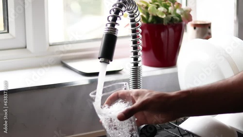 Person filling glass by tap water. Holding glass under running faucet.  Ecological and healthy drink, wide angle using 2 hands
