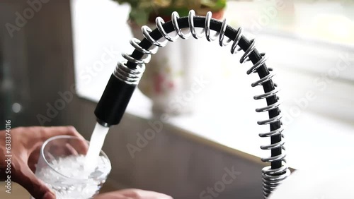 Person filling glass by tap water. Holding glass under running faucet.  Ecological and healthy drink. close up