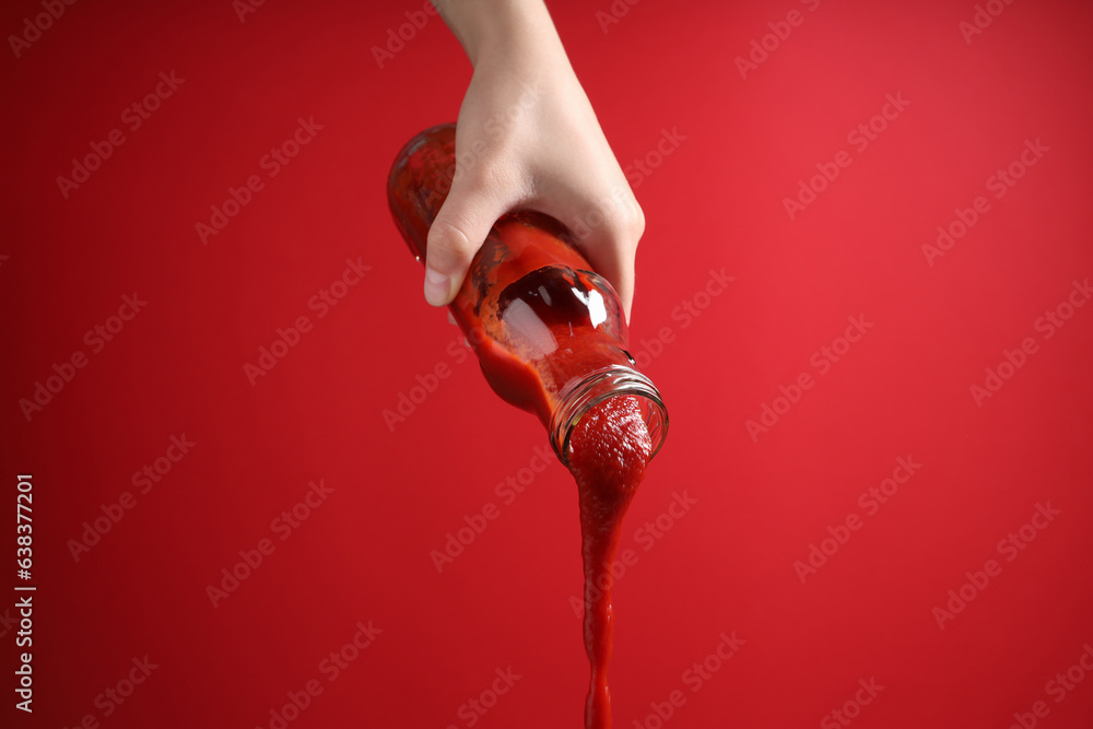 Woman pouring tasty ketchup from bottle on red background, closeup Woman pouring tasty ketchup from bottle on red background, closeup