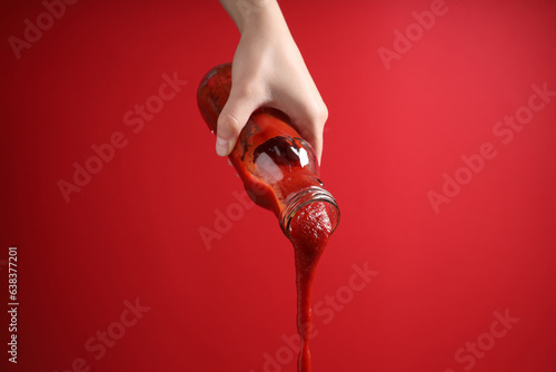 Woman pouring tasty ketchup from bottle on red background, closeup © New Africa