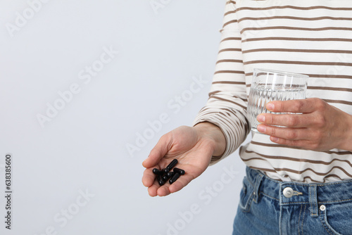 Fotografie A woman is holding tablets of activated charcoal on a light background