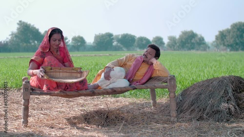 Indian village couple in their field - sitting on a Chaarpai  wheat field  village lifestyle  happy Indian couple. Mid aged Indian desi man wearing kurta pyjama is relaxing and his wife in saree cl... photo