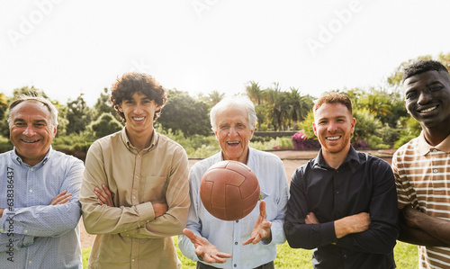 Multi generational men smiling in front of camera - Male multiracial group playing soccer with vintage ball during sunday day at city park - Main focus on center senior man face