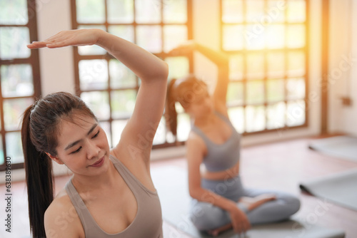Fototapeta Naklejka Na Ścianę i Meble -  Asian sporty women practicing yoga for beginners in yoga studio, wellbeing healthy stretching concept. Asian women exercising in yoga fitness studio.