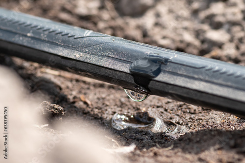 Close up of drip irrigation on a field, macro shot. Drop of water on the part of irrigation system in the garden, concept of smart gardening