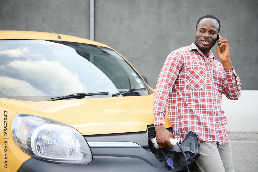 A african american man stands next to yellow electric delivery van at electric vehicle charging stations A african american man stands next to yellow electric delivery van at electric vehicle charging stations