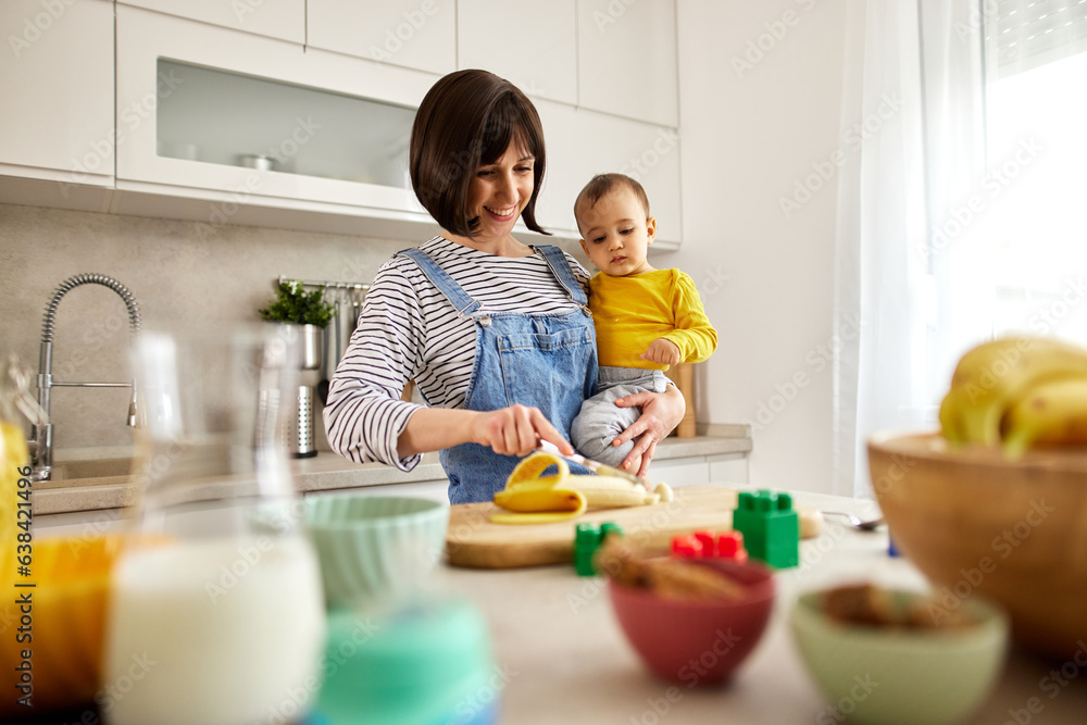 Mother feeding her baby boy with banana in the kitchen