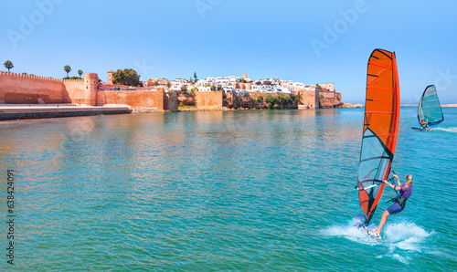 Foto Windsurfer Surfing The Wind On Waves - Kasbah of Udayas fortress in Rabat Morocco