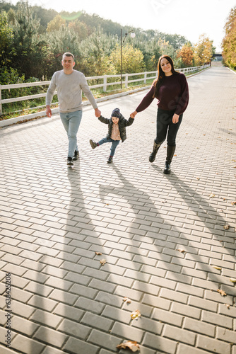 Mom, dad hold hands daughter child walking in park. Family spending time together at sunset on vacation, autumn holiday. Mother, father, kid running in street in nature. View on legs silhouette.