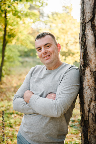 Fototapeta Naklejka Na Ścianę i Meble -  Male walks in yellow leaves in forest. Portrait man, father near tree in an autumn park. Family spending time at sunset on vacation. Autumn holiday in nature. Closeup. Spring mood photo with sunlight